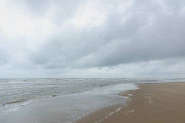 Winter landscape, Sand beach and sea wave under white grey cloudy clouds in sky, The dunes or dyke along Dutch north sea coastline between Petten and Callantsoog in North Holland, Netherlands. - Powered by Adobe