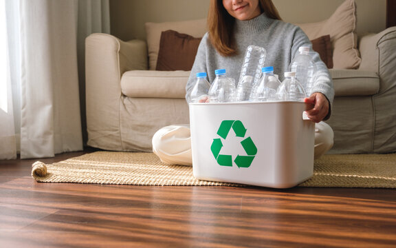 Closeup image of a young woman collecting and separating recyclable garbage plastic bottles into a trash bin at home