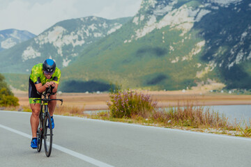 Full length portrait of an active triathlete in sportswear and with a protective helmet riding a bicycle. Selective focus  - obrazy, fototapety, plakaty