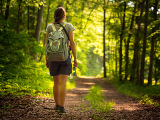 A young woman with backpack hiking on a bright forest path on a hot summer's day | forest hike in Germany | outdoor tourism thuringia - obrazy, fototapety, plakaty