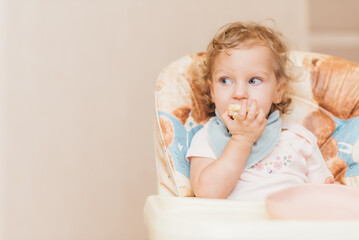 Fototapeta premium Happy little baby eats at home sitting on a chair
