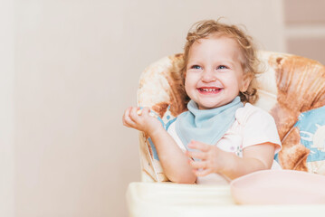 Fototapeta premium Happy little baby eats at home sitting on a chair