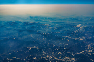 View from the airplane window at the setting sun and mountains crossed by clouds