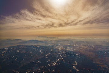 View from the airplane window at the setting sun and mountains crossed by clouds