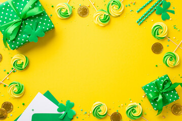 Saint Patrick's Day concept. Top view photo of green gift boxes meringue candies sprinkles gold coins envelope with card straws clovers on isolated vivid yellow background with copyspace in the middle