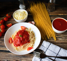 Spaghetti or pasta with tomato sauce, on a white plate on a dark wooden background with tomatoes.