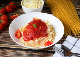 Spaghetti or pasta with tomato sauce, on a white plate on a dark wooden background with tomatoes.