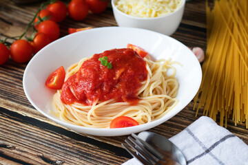 Spaghetti or pasta with tomato sauce, on a white plate on a dark wooden background with tomatoes.