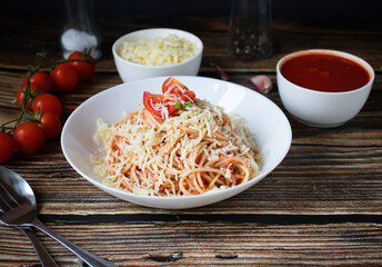 Spaghetti or pasta with tomato sauce, on a white plate on a dark wooden background with tomatoes.