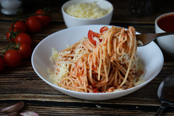 Spaghetti or pasta with tomato sauce, on a white plate on a dark wooden background with tomatoes.