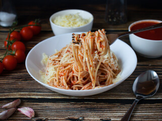 Spaghetti or pasta with tomato sauce, on a white plate on a dark wooden background with tomatoes.