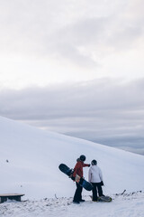 A snowboarder in a red jacket stands on top of a mountain and looks into the distance