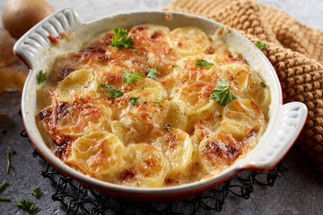 Ceramic dish of potato gratin with grated cheese and parsley