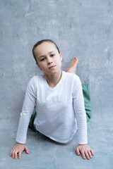 Selective focus vertical portrait of cute serious-looking blond little girl stretching on concrete background