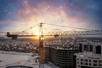 Fototapeta premium Industrial cranes at construction site with dramatic sunset sky background.