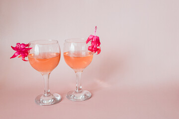 two glasses of rose wine or champagne on a pink background with bright scarlet flowers inside