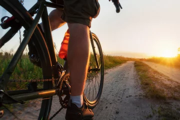Foto op Aluminium Man riding a gravel bicycle on the trail at sunset. Colorful landscape with cyclist, bike, field, green grass and bright sunlight. Sport and travel. close up view. © Артур Ничипоренко