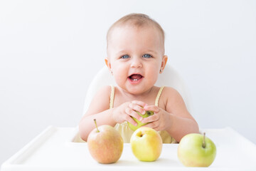 Fototapeta premium cute baby girl in baby chair eating apples. Baby first solid food