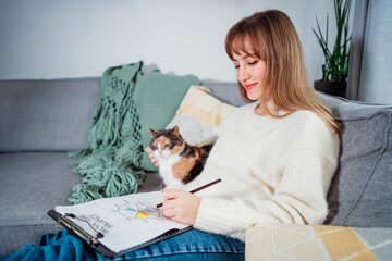 Relaxed young woman drawing work-life balance wheel sitting on the sofa with cat pet at home....