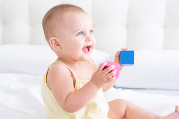 funny baby girl in yellow bodysuit playing with children wooden cubes on bed