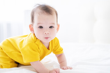 healthy asian baby girl 5 months in yellow bodysuit on bed on white bedding