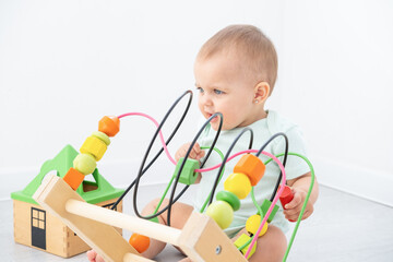 cute baby girl in bodysuit playing with colorful wooden toys on white room