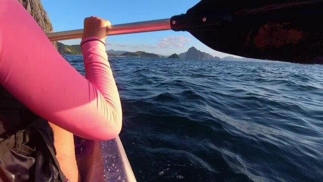 Rear view of a woman kayaker paddling in the sea at the beginning of sunset. Active lifestyle concept