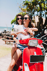 Close up outdoor photo of two stylish pretty girls in sunglasses, caps and white t-shirts sitting...