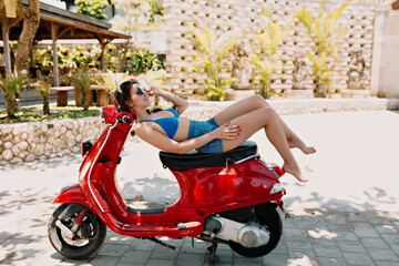 Fototapeta na wymiar Full-lenght outdoor photo of attractive pretty woman wearing swim suit and shorts lying on the red bike and resting in sunny warm summer day