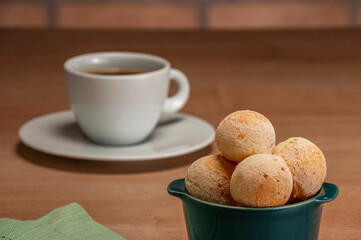 Cheese breads in a green ramekin with a cup of coffee on wooden table and bricks wall background.