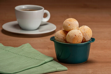Cheese breads in a green ramekin with a cup of coffee on wooden table.