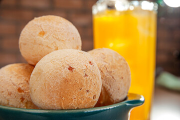 Cheese breads in a green ramekin with a glass of orange juice on wooden table and bricks wall background.