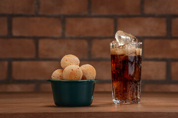Cheese breads in a green ramekin with a glass of cola soft drink on wooden table and bricks wall...