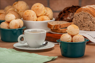 Cheese breads in a green ramekin with a cup of coffee on wooden table and bricks wall background.