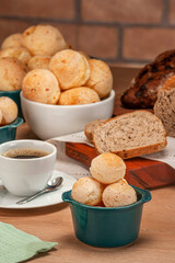 Cheese breads in a green ramekin with a cup of coffee on wooden table and bricks wall background.