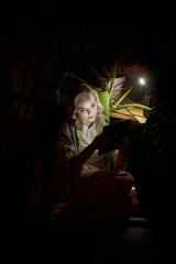 Young beautiful woman sitting in dark room sitting on chair with laptop at home in the evening with...