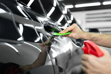 Car service worker glues anti-gravity film on the car body with a scraper in car detailing workshop