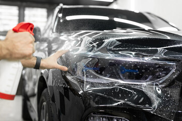 Worker applies a protective film or anti-gravity protective coating to the car headlight. Details...