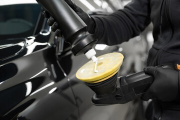 Professional detailing of the car in the auto studio, the master applies paste or wax to the car body polishing machine.