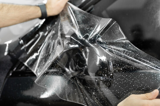 Man applying sticking protective film on car mirror at the vehicle service station. Detailing studio