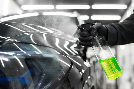 Master sprays aerosol wax on the surface of the car before polishing. Detailing studio.