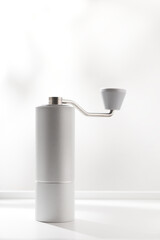 Vertical photo of light gray manual coffee grinder on white table.