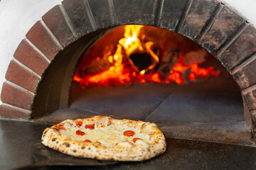 Italian pizza is cooked in a wood-burning oven. The cook puts the pizza in the oven on a shovel.