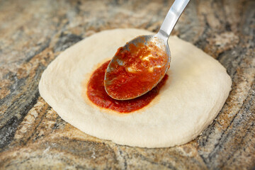 A man adding tomato sauce to the base of an Italian pizza. Cooking pizza in a pizzeria.