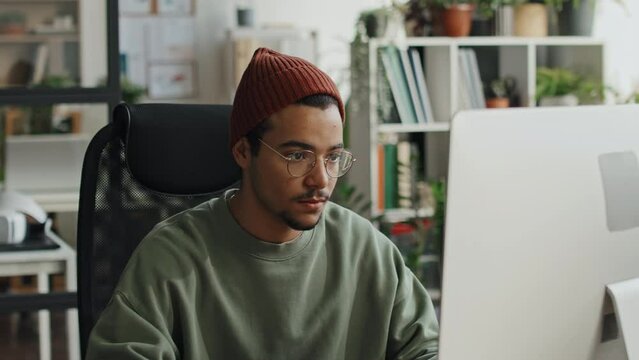 Medium close-up of young developer working with software on computer while sitting at his workplace in modern office