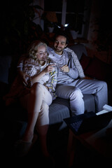 Cheers. Romantic date night. Young man and woman sitting together on couch at home in the evening...
