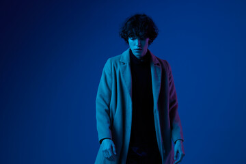 Male model in fashion coat on dark blue background, neon light, style and trends, mixed light, men's fashion