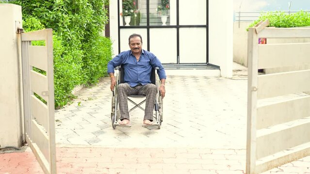 Lonely Indian senior, elder, widower living with disability, rolling wheelchair outside old age home. Retired male go out of rehabilitation clinic for leisure activity. Health care illness old age