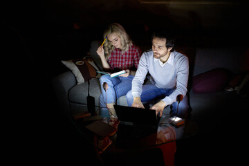 Freelance, education. Man and woman, couple sitting on sofa at home in the evening and studying,...