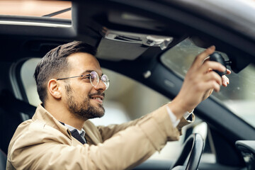 A young happy businessman is adjusting rear view mirror in a car.